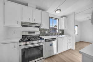 Kitchen featuring sink, light wood-type flooring, appliances with stainless steel finishes, decorative backsplash, and white cabinetry