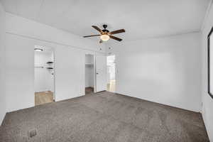 Unfurnished bedroom with a walk in closet, ensuite bath, a closet, ceiling fan, and light colored carpet