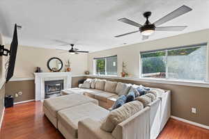 Living room with ceiling fan, a textured ceiling, a tiled fireplace, and wood-type flooring