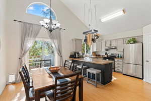 Dining space with high vaulted ceiling, an inviting chandelier, and light hardwood / wood-style flooring