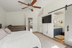 Bedroom with ceiling fan, light wood-type flooring, a barn door, ensuite bathroom, and lofted ceiling