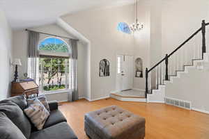 Living room with high vaulted ceiling, light hardwood / wood-style floors, and a chandelier