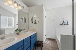 Bathroom featuring tile patterned flooring, a bathing tub, dual vanity, and lofted ceiling