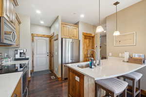 Kitchen featuring dark hardwood / wood-style floors, a kitchen breakfast bar, appliances with stainless steel finishes, hanging light fixtures, and sink