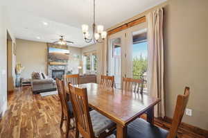 Dining area with ceiling fan with notable chandelier, a fireplace, and wood-type flooring