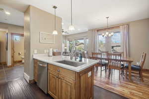 Kitchen with dark hardwood / wood-style floors, ceiling fan with notable chandelier, dishwasher, hanging light fixtures, and sink