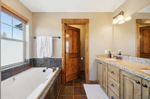 Bathroom with tile patterned flooring, a relaxing tiled tub, and vanity