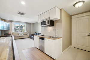 Kitchen with white cabinets, appliances with stainless steel finishes, light colored carpet, and sink