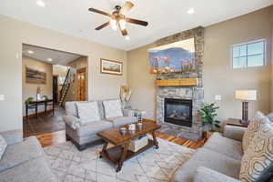 Living room with ceiling fan, a stone fireplace, and hardwood / wood-style flooring