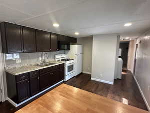 Kitchen with decorative backsplash, dark hardwood / wood-style flooring, sink, white appliances, and dark brown cabinets