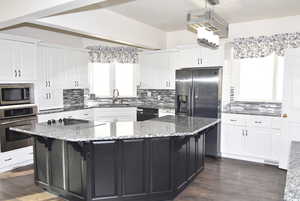 Kitchen with white cabinetry, stone counters, sink, a spacious island, and black appliances