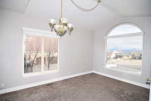 Carpeted empty room with lofted ceiling and a chandelier