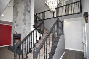 Staircase featuring a fireplace, a high ceiling, a notable chandelier, and hardwood / wood-style floors