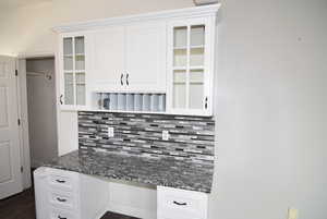 Kitchen with white cabinets, decorative backsplash, built in desk, and dark stone counters