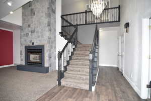 Staircase featuring hardwood / wood-style floors, a large fireplace, high vaulted ceiling, and a notable chandelier