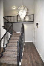 Stairway with a towering ceiling, a chandelier, and hardwood / wood-style flooring