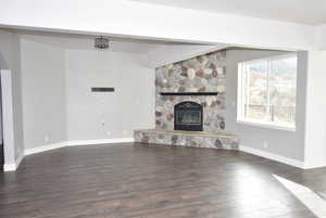 Unfurnished living room with a stone fireplace and dark hardwood / wood-style floors