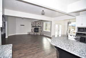 Kitchen with dark hardwood / wood-style flooring, stainless steel appliances, a fireplace, white cabinetry, and hanging light fixtures