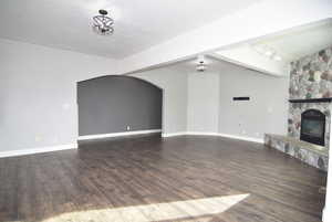 Unfurnished living room featuring a fireplace, beam ceiling, dark hardwood / wood-style flooring, and a textured ceiling