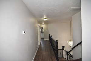 Hall featuring a textured ceiling, a notable chandelier, and dark wood-type flooring