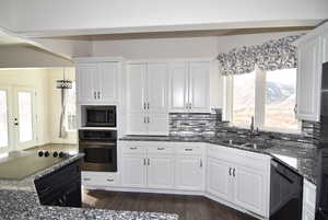 Kitchen with dark stone countertops, sink, white cabinets, and black appliances