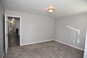 Unfurnished room featuring a textured ceiling and dark carpet