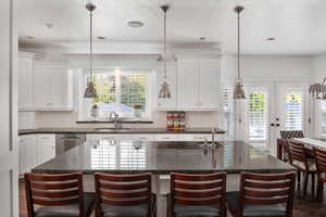 Kitchen with sink, dishwasher, white cabinetry, hanging light fixtures, and a center island with sink