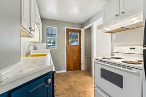 Kitchen featuring decorative backsplash, white stove, white cabinetry, sink, and light tile patterned flooring