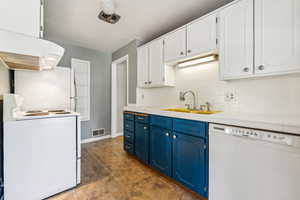 Kitchen with blue cabinets, backsplash, custom range hood, white appliances, and tile patterned flooring