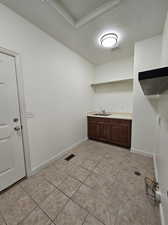 Clothes washing area featuring light tile patterned flooring, sink, and a textured ceiling