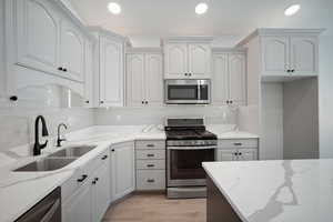 Kitchen featuring appliances with stainless steel finishes, light stone counters, tasteful backsplash, and light hardwood / wood-style flooring