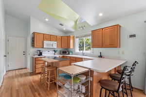 Kitchen featuring sink, high vaulted ceiling, light hardwood / wood-style floors, a breakfast bar area, and kitchen peninsula