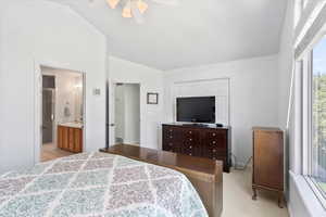 Carpeted bedroom featuring ceiling fan, vaulted ceiling, sink, and ensuite bathroom