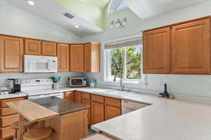 Kitchen featuring a kitchen bar, sink, high vaulted ceiling, white appliances, and kitchen peninsula