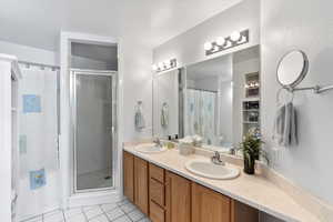 Bathroom with toilet, double vanity, tile patterned flooring, and a shower with shower door