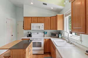 Kitchen with light wood-type flooring, vaulted ceiling, sink, and white appliances