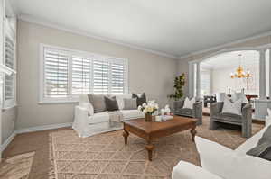 Carpeted living room featuring ornamental molding, an inviting chandelier, and ornate columns