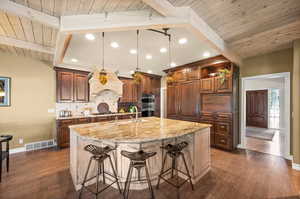 Kitchen featuring decorative backsplash, hanging light fixtures, an island with sink, a breakfast bar, and beamed ceiling