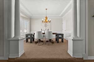 Carpeted dining area with ornate columns, an inviting chandelier, and ornamental molding