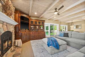 Living room with ceiling fan, beam ceiling, a stone fireplace, and wood ceiling