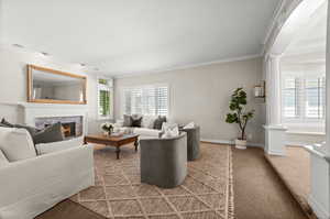 Living room with ornate columns, ornamental molding, light colored carpet, and a premium fireplace