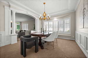 Carpeted dining area featuring a tray ceiling, a notable chandelier, ornamental molding, and decorative columns