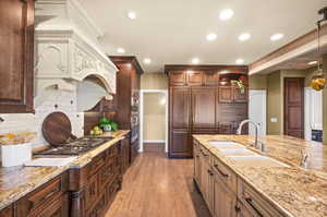 Kitchen with backsplash, stainless steel gas cooktop, sink, hardwood / wood-style flooring, and hanging light fixtures