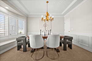 Carpeted dining area with a notable chandelier, a raised ceiling, and crown molding