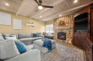 Carpeted living room featuring ceiling fan, beam ceiling, a stone fireplace, and wood ceiling