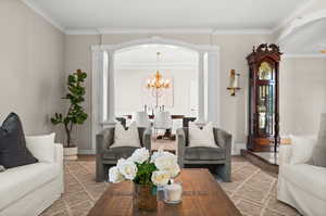 Living room with crown molding, decorative columns, and a notable chandelier