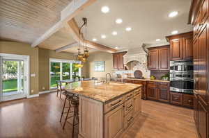 Kitchen featuring appliances with stainless steel finishes, premium range hood, tasteful backsplash, an island with sink, and hardwood / wood-style flooring