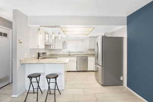 Kitchen with light stone countertops, light tile patterned floors, stainless steel appliances, kitchen peninsula, and white cabinets