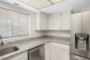 Kitchen with white cabinets, sink, appliances with stainless steel finishes, and light stone counters