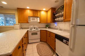 Kitchen with sink, decorative backsplash, white appliances, and light tile patterned floors